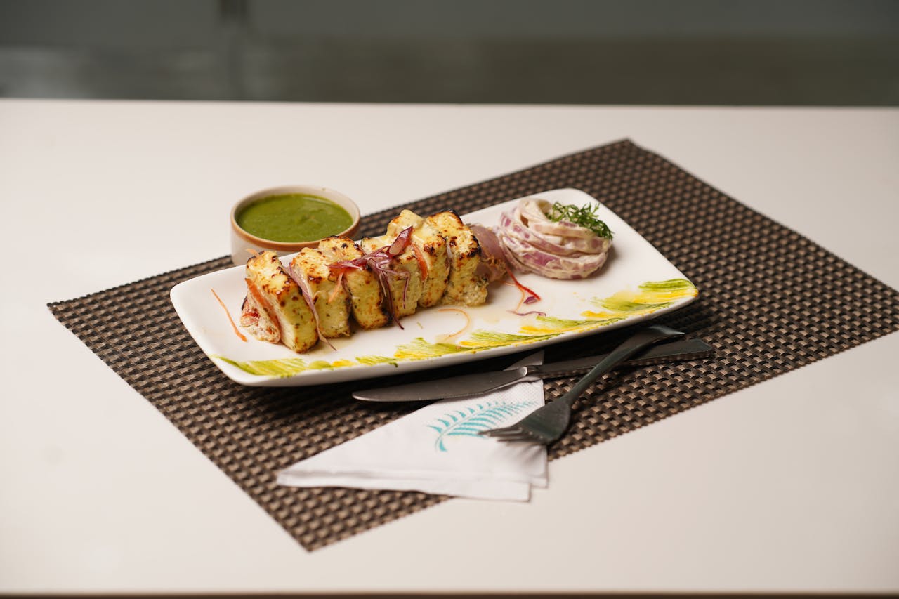 Plate of flavorful paneer tikka served with mint chutney and onion salad on a table.